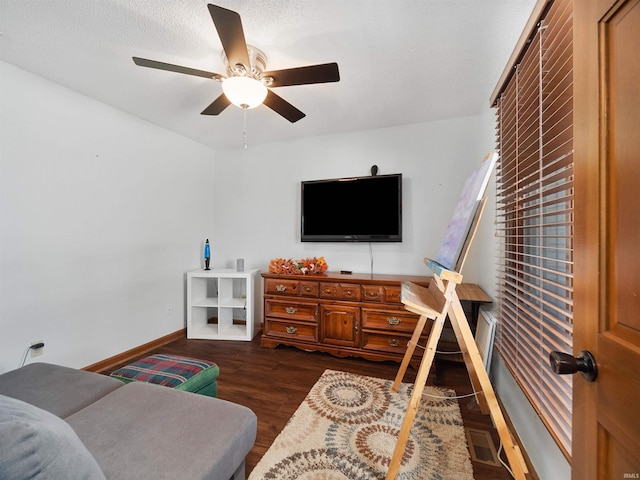 interior space with a textured ceiling, ceiling fan, visible vents, baseboards, and dark wood finished floors