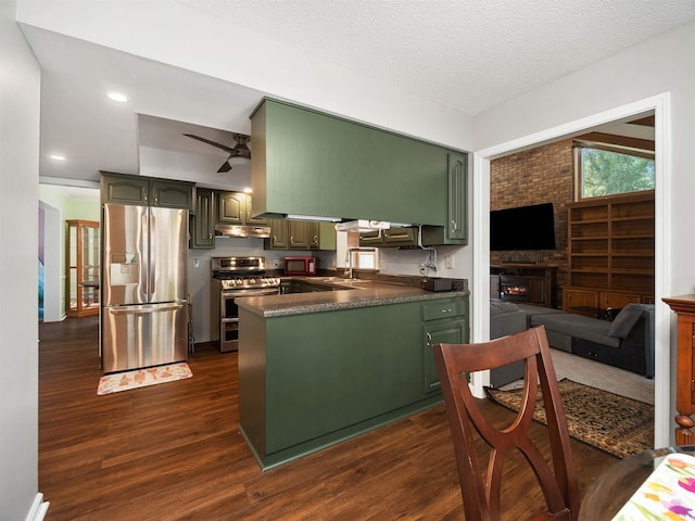 kitchen featuring dark countertops, a peninsula, stainless steel appliances, under cabinet range hood, and a sink