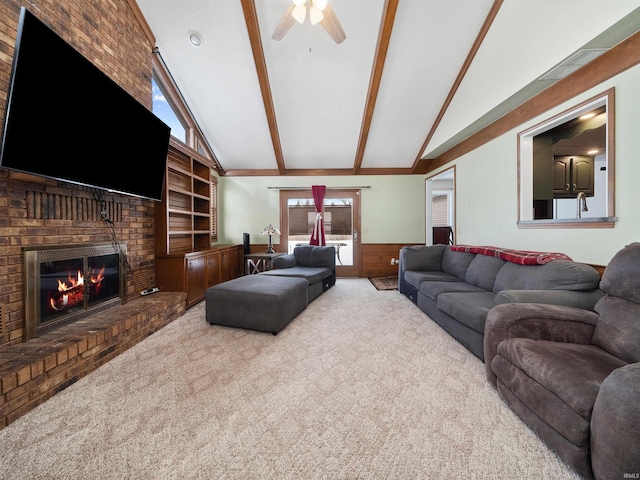 carpeted living area featuring lofted ceiling with beams, a fireplace, a ceiling fan, and wainscoting