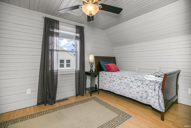 bedroom featuring ceiling fan, hardwood / wood-style floors, and wooden walls