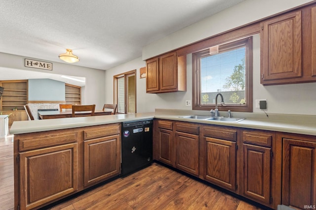 kitchen featuring a sink, black dishwasher, light countertops, dark wood-type flooring, and a peninsula