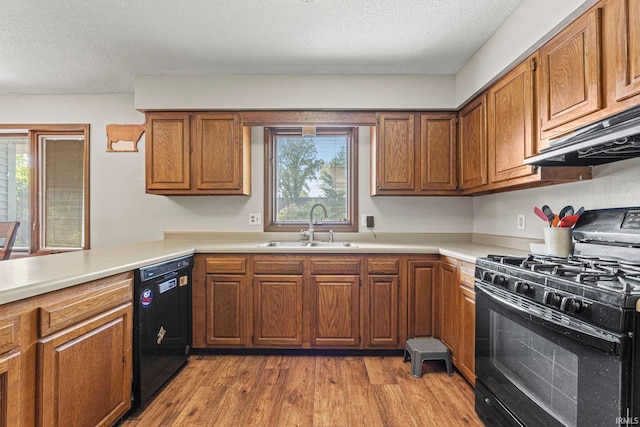 kitchen with light countertops, a sink, black appliances, brown cabinetry, and under cabinet range hood