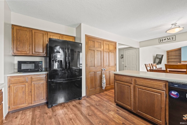 kitchen with light wood-style flooring, light countertops, brown cabinets, a textured ceiling, and black appliances