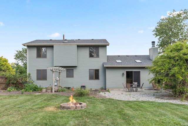 back of house with a lawn, a patio area, a fire pit, a shingled roof, and a chimney