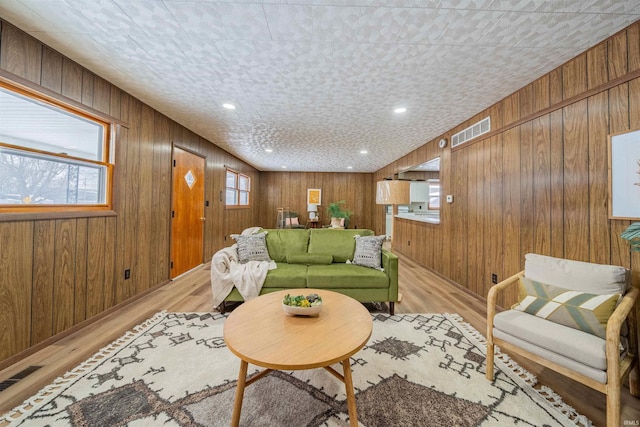 living area with visible vents, light wood-style floors, and wood walls