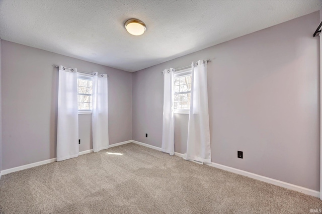 spare room featuring a healthy amount of sunlight, a textured ceiling, baseboards, and carpet flooring