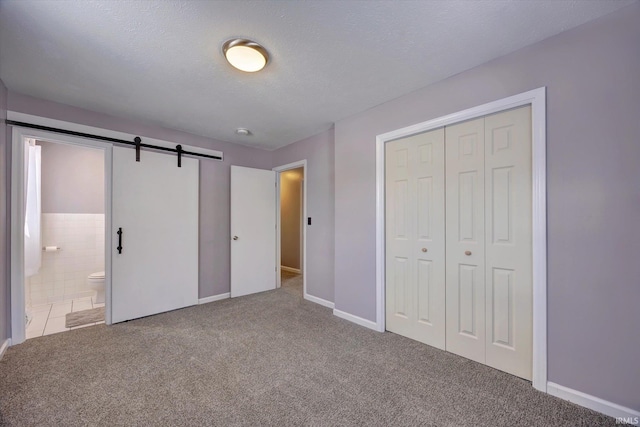 unfurnished bedroom with a barn door, connected bathroom, carpet, a textured ceiling, and a closet