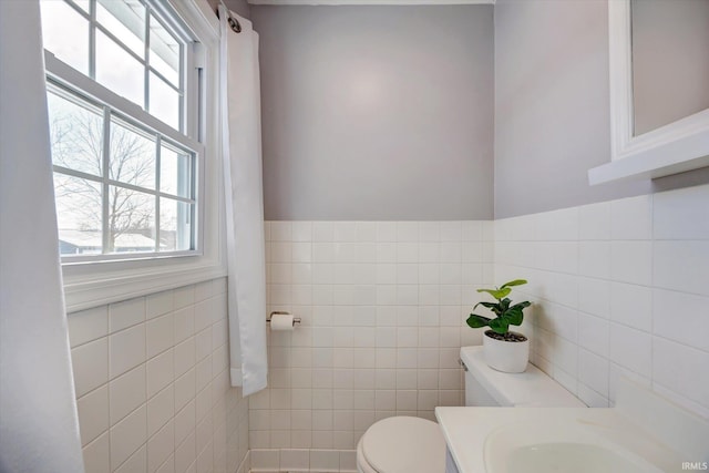 half bath featuring a wainscoted wall, tile walls, toilet, and vanity