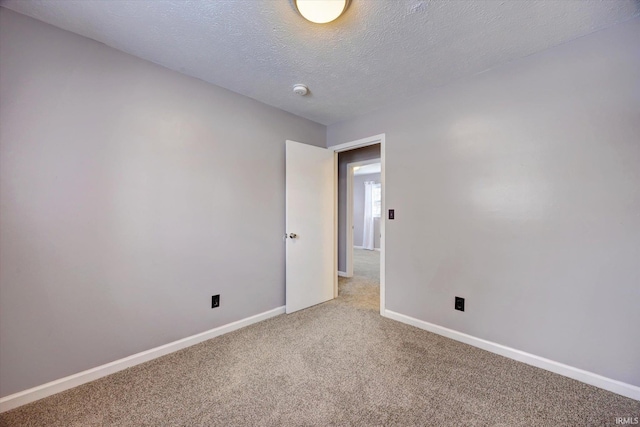 empty room featuring a textured ceiling, carpet, and baseboards