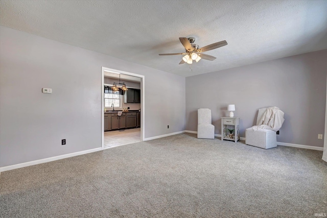 unfurnished room with baseboards, light colored carpet, ceiling fan, a textured ceiling, and a sink