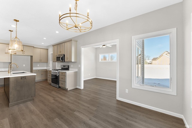 kitchen with a sink, baseboards, light countertops, appliances with stainless steel finishes, and hanging light fixtures