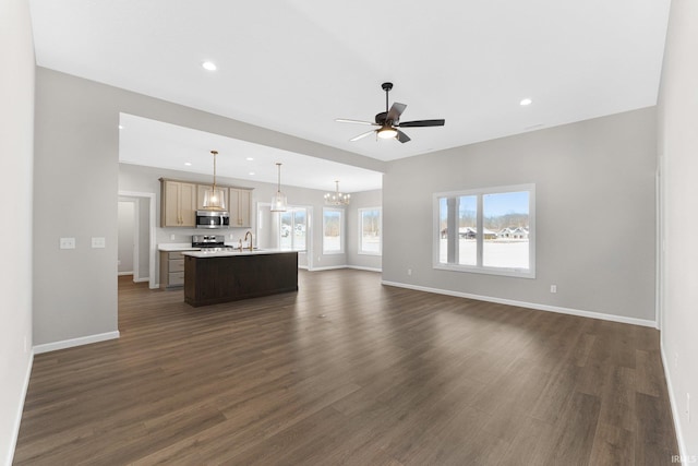 unfurnished living room featuring baseboards, dark wood-type flooring, ceiling fan with notable chandelier, a sink, and recessed lighting