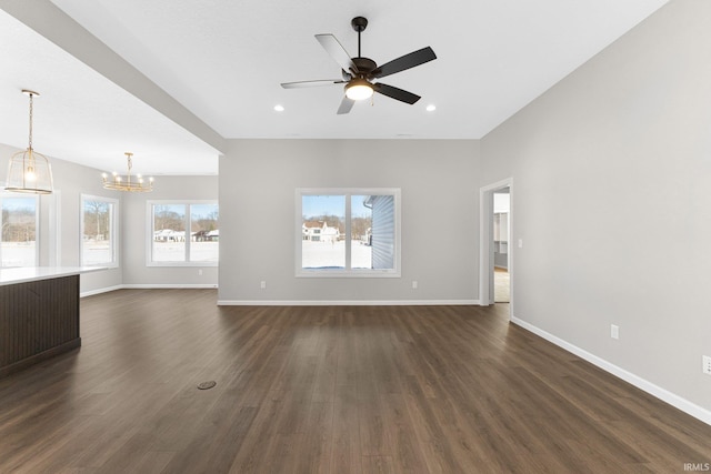 unfurnished living room with dark wood-type flooring, recessed lighting, baseboards, and ceiling fan with notable chandelier