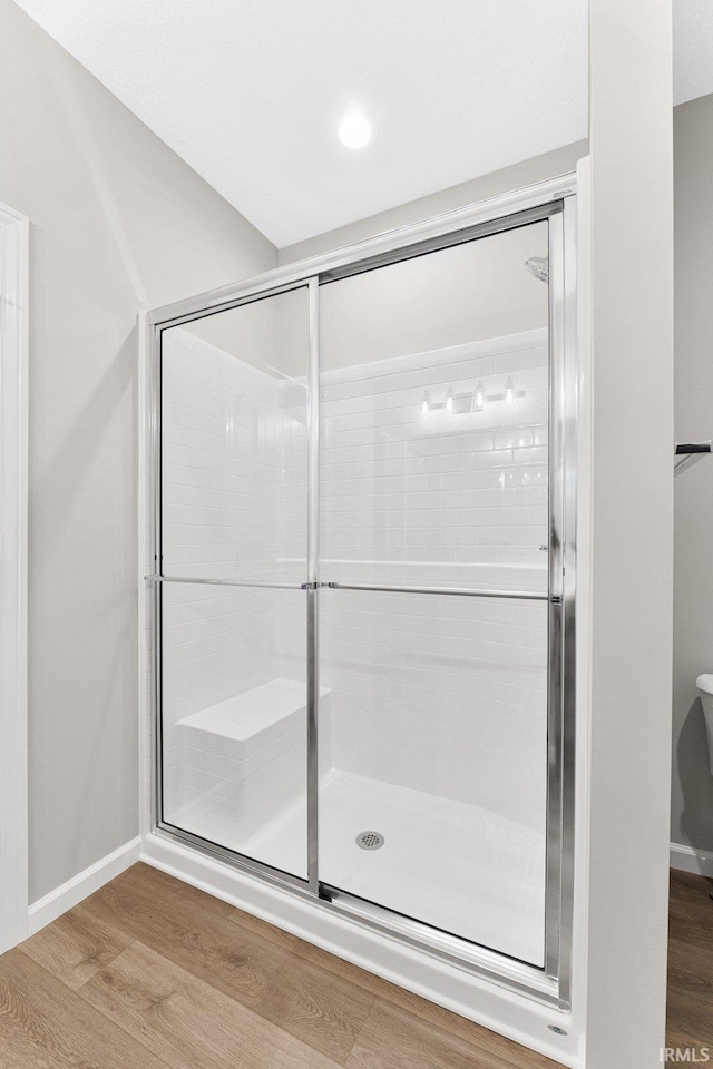 bathroom with wood finished floors, a shower with shower door, and baseboards