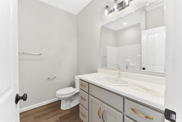 bathroom featuring toilet, wood finished floors, vanity, baseboards, and walk in shower