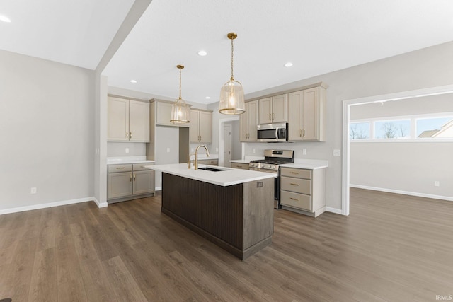 kitchen with pendant lighting, stainless steel appliances, light countertops, a sink, and an island with sink