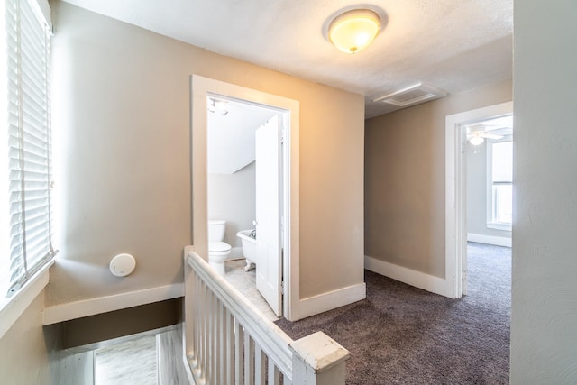 hallway with visible vents, baseboards, and dark colored carpet