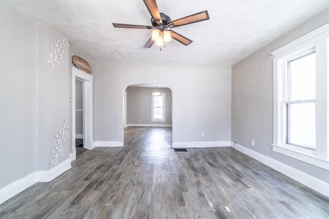 unfurnished room with arched walkways, dark wood-type flooring, a ceiling fan, and baseboards