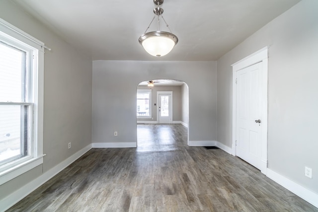 spare room featuring dark wood-style floors, arched walkways, and baseboards