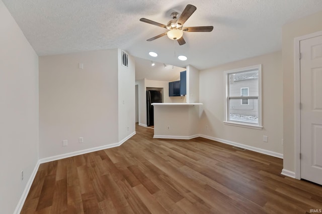 unfurnished living room with dark wood-style flooring, visible vents, a textured ceiling, and baseboards