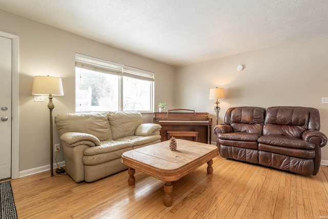 living room featuring a textured ceiling, baseboards, and light wood-style floors