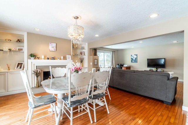 dining space with built in shelves, recessed lighting, a textured ceiling, wood finished floors, and a chandelier