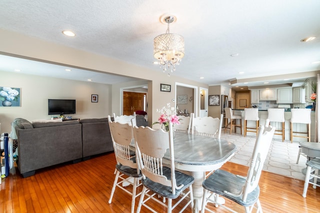 dining space with a textured ceiling, recessed lighting, wood finished floors, and an inviting chandelier