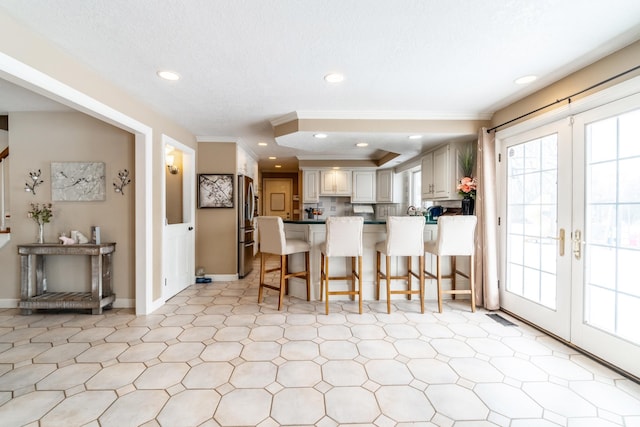 kitchen with tasteful backsplash, visible vents, a kitchen breakfast bar, freestanding refrigerator, and crown molding