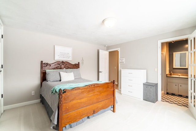 bedroom featuring light colored carpet, a sink, baseboards, and ensuite bathroom