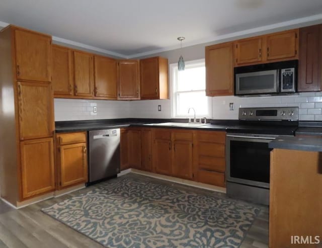 kitchen featuring appliances with stainless steel finishes, dark countertops, decorative light fixtures, and brown cabinets