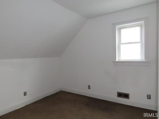 additional living space with dark colored carpet, visible vents, vaulted ceiling, and baseboards