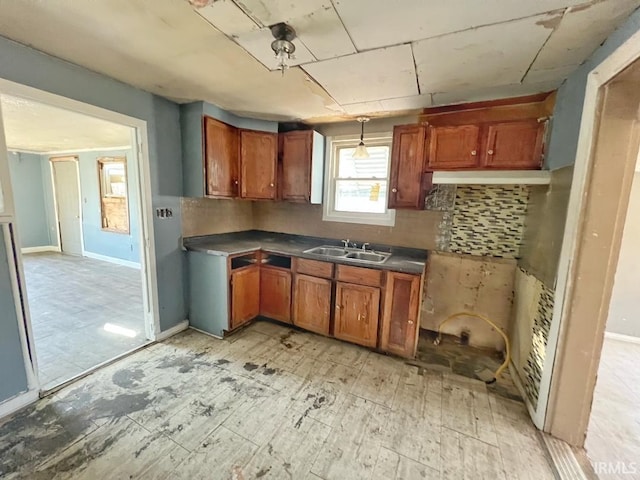 kitchen featuring baseboards, dark countertops, brown cabinets, a sink, and backsplash