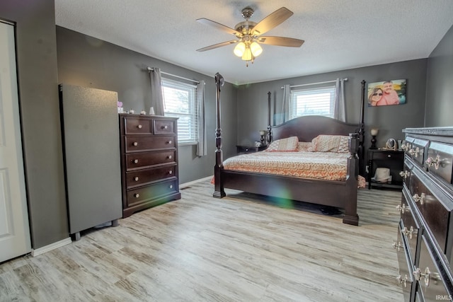 bedroom with a textured ceiling, ceiling fan, multiple windows, and light wood-type flooring