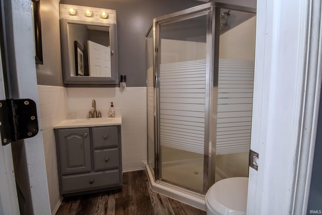 bathroom with a stall shower, wainscoting, wood finished floors, vanity, and tile walls