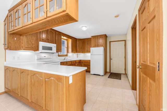 kitchen featuring a peninsula, white appliances, light countertops, brown cabinetry, and glass insert cabinets