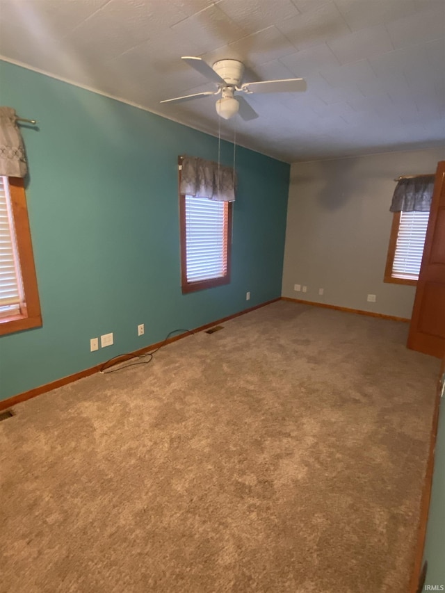 empty room with carpet floors, visible vents, baseboards, and a ceiling fan