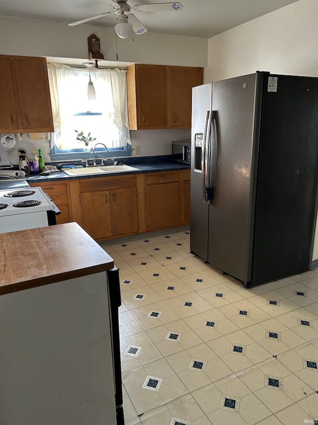 kitchen featuring stainless steel fridge, electric range oven, dark countertops, brown cabinets, and a sink