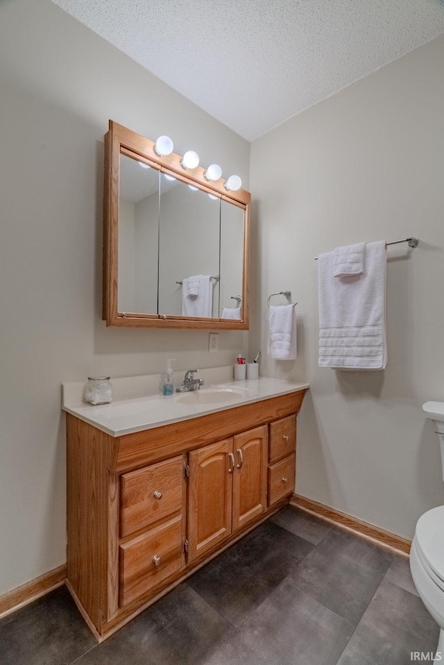 bathroom with baseboards, vanity, toilet, and a textured ceiling