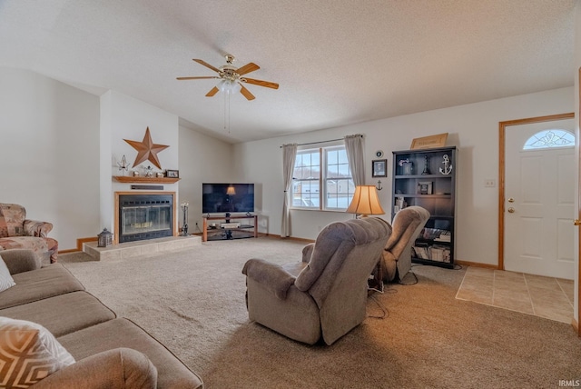 living area with ceiling fan, a textured ceiling, lofted ceiling, light carpet, and a tiled fireplace