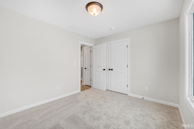 unfurnished bedroom with baseboards, multiple windows, a closet, and light colored carpet