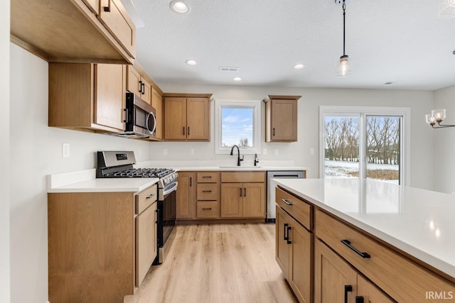 kitchen with pendant lighting, stainless steel appliances, light countertops, light wood-style flooring, and a sink