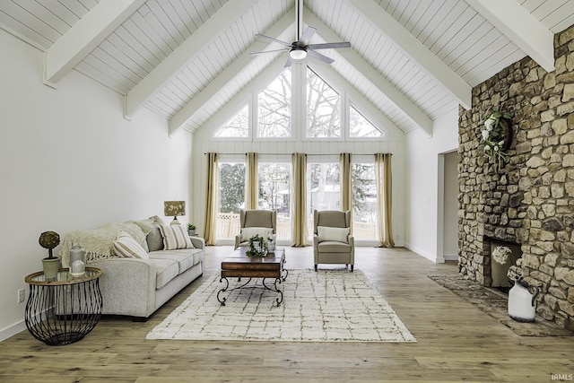 living area with high vaulted ceiling, a stone fireplace, light wood-style flooring, and beam ceiling