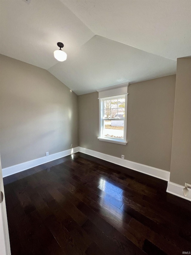 unfurnished room with dark wood finished floors, vaulted ceiling, and baseboards