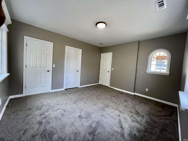 unfurnished bedroom with visible vents, dark carpet, and baseboards