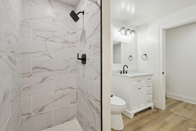 bathroom featuring toilet, a tile shower, vanity, wood finished floors, and baseboards