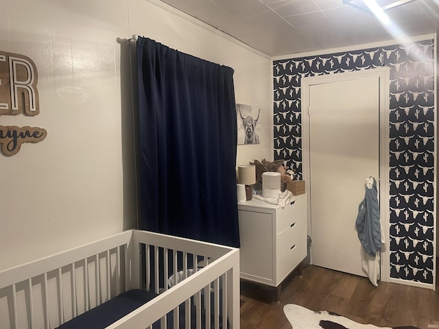 bedroom with a nursery area, crown molding, and dark wood-style flooring