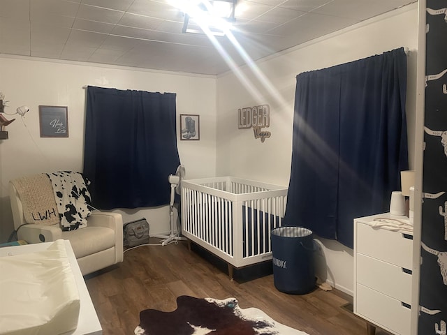 bedroom with dark wood finished floors and a crib