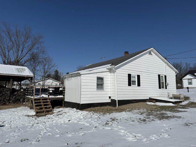 snow covered back of property featuring a chimney and cooling unit