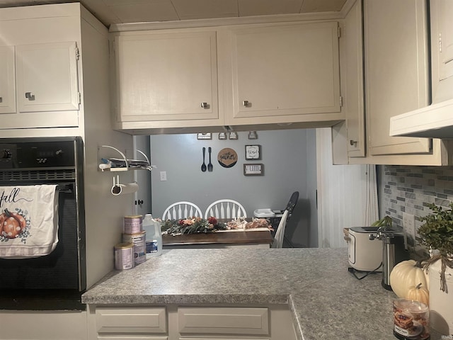 kitchen with tasteful backsplash, white cabinets, and oven