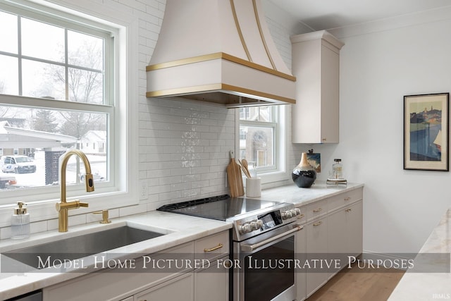 kitchen featuring premium range hood, a sink, white cabinetry, stainless steel range with electric cooktop, and backsplash